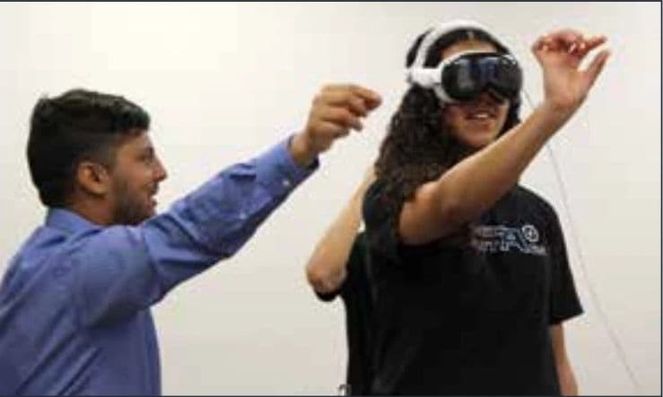 Sujan Ghimire guiding a student who is wearing a virtual reality headset in a classroom.